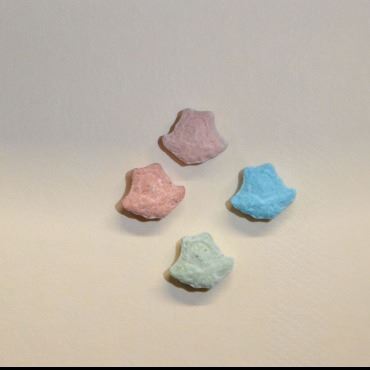 Baggie and individual colorful, vitamin looking pills. Shape looks like an animal face.