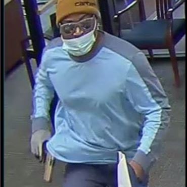 Thin black man in dark pants, light blue long sleeve shirt, brown Carhartt hat, with glasses.