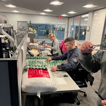Police staff sitting at cubicle desks, wrapping presents.