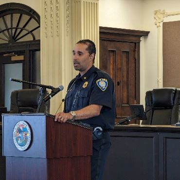 Man in a police uniform speaking at a podium.
