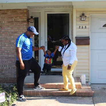 Man and woman swinging child by the hands down the front stoop of a house.